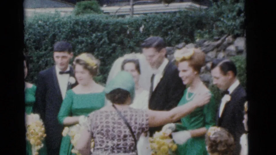 1961 Camden wedding-party moment showing a woman in a green hat greeting a bridesmaid while the bride and attendants stand nearby.