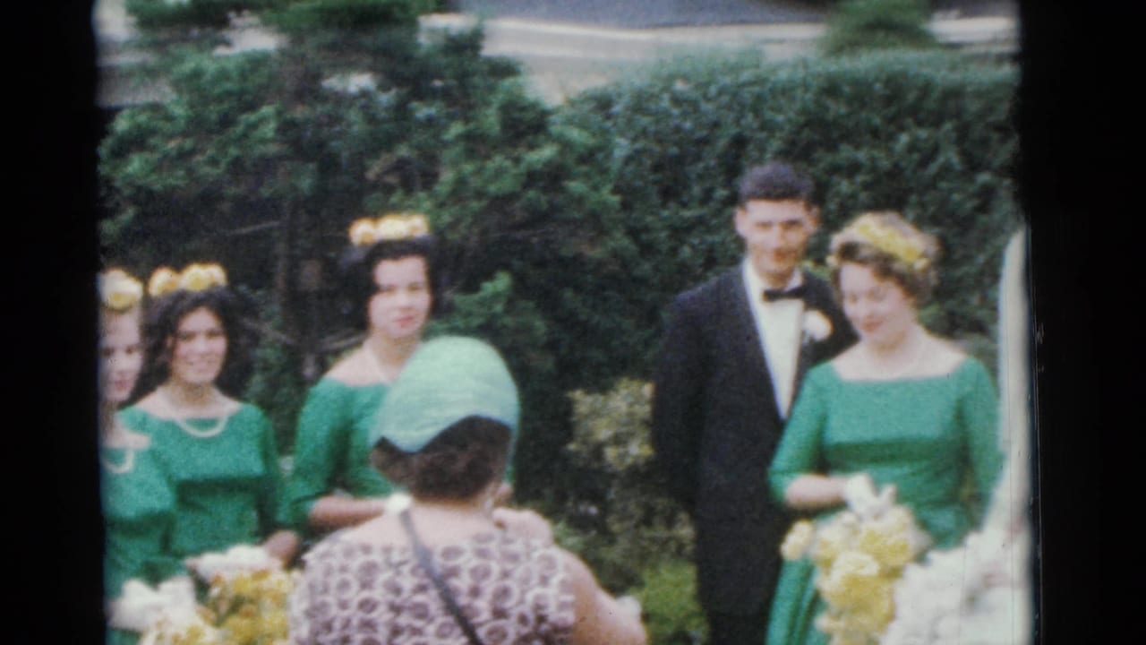 Bride, groom, bridesmaid, and best man stand together outdoors with guests partly visible.