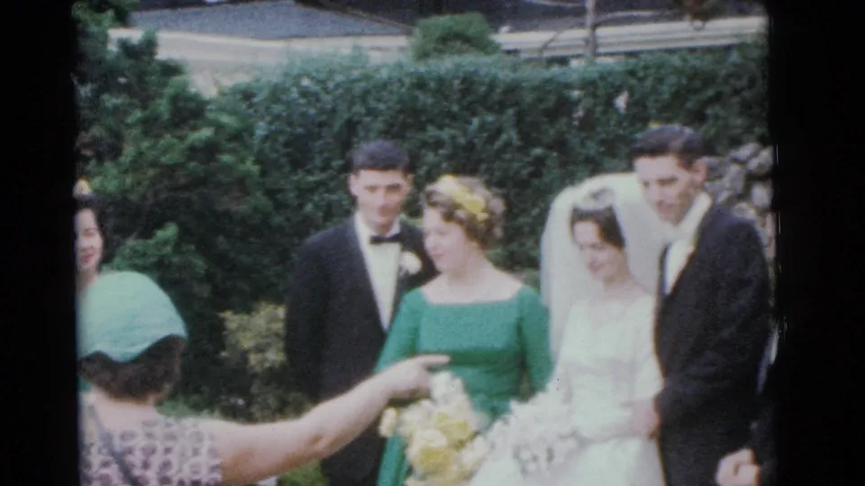Outdoor 1961 Camden wedding frame with a gesturing guest or organizer directing the bride, groom, and attendants during a group pose.