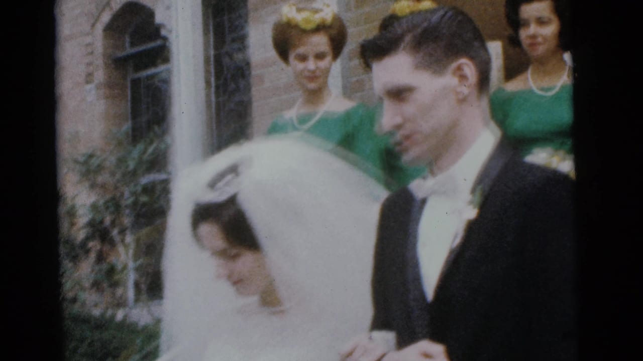 Bride in a white veil and groom in a black tuxedo stand outside a brick church with bridesmaids behind them.