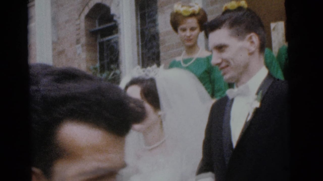 Groom smiles beside the bride while a bridesmaid stands behind them outside the church.