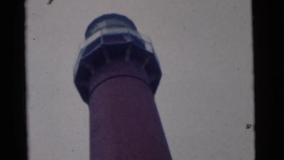1961 8mm Camden frame showing the lantern room and railing of a red lighthouse from a steep low angle.