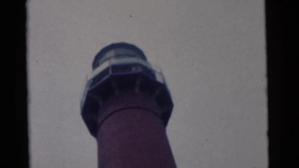 Final 1961 Camden frame holding on the lighthouse lantern room and red tower against an overcast sky.