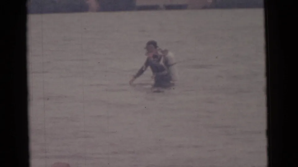1961 Camden, New Jersey home-movie frame showing a male scuba diver wading in shallow water with a light tank.