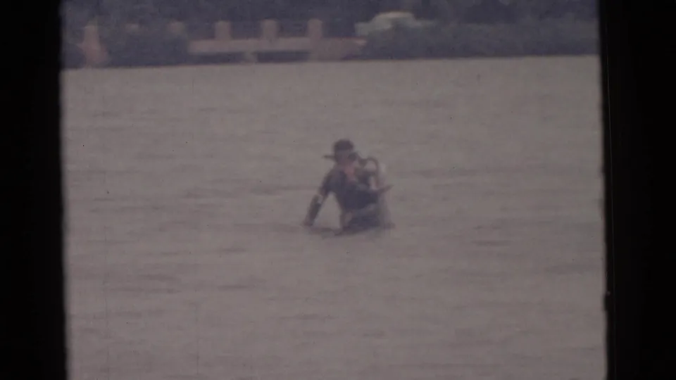 A male scuba diver in a dark suit and light tank appears farther from the camera in Camden waterfront footage from 1961.