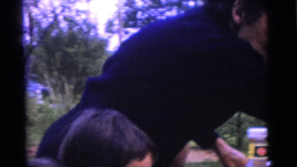 1961 Camden backyard frame with a dark-clothed adult partly blocking the view as another nearby figure appears at the lower edge.