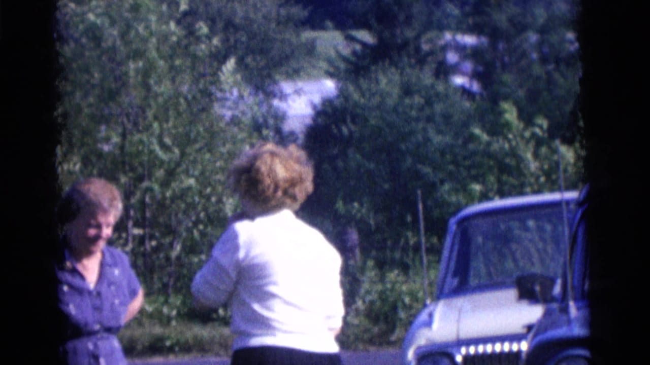 In 1961 Camden, New Jersey home-movie footage, two adult women talk beside a road with a classic car partly visible.