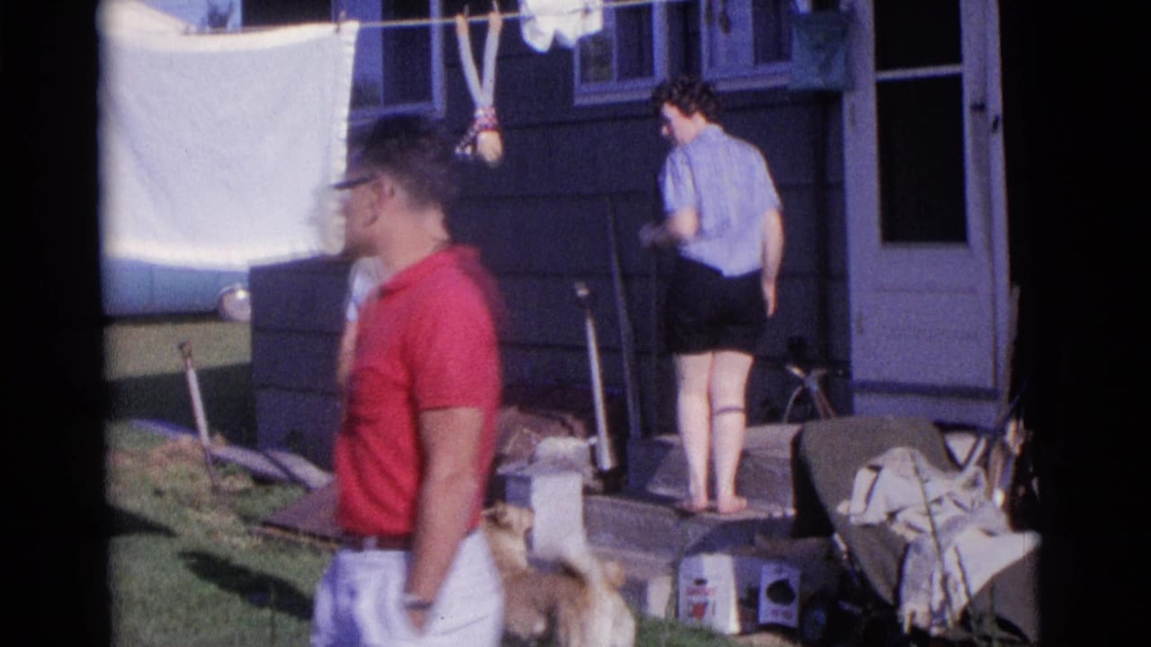 Adults in a yard beside a house with laundry on a clothesline and a dog near the grass.