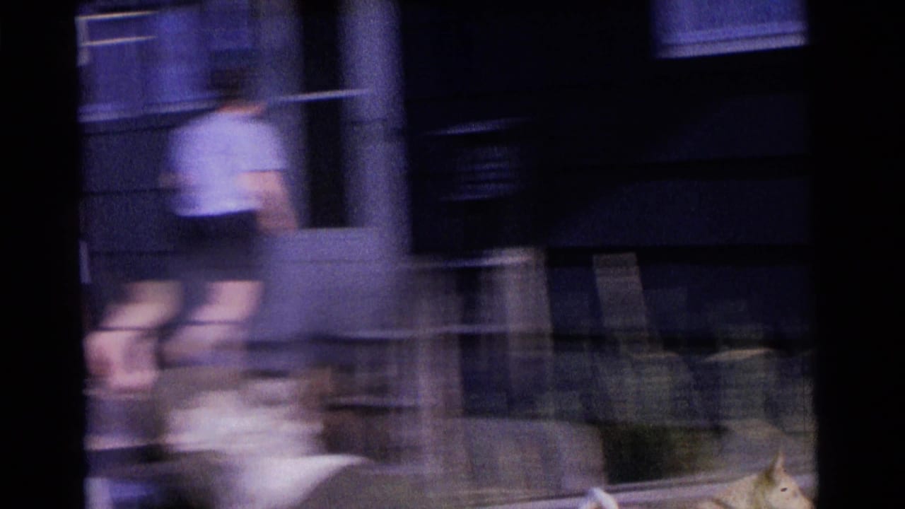 Motion-blurred 1961 Camden yard view with an adult near a house exterior and outdoor objects partly visible.