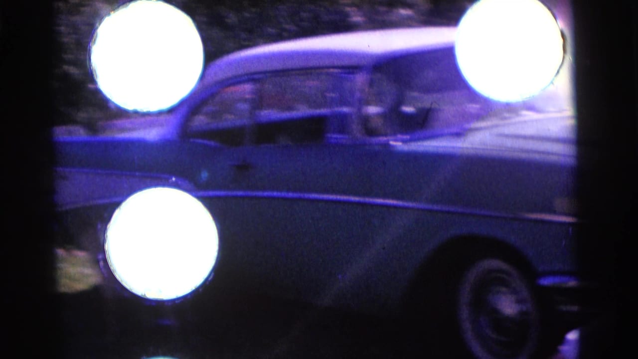 Blue vintage sedan passing through a dark 8mm frame with bright circular film artifacts.