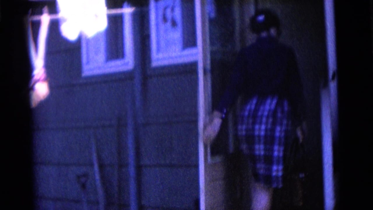 In Camden, New Jersey home-movie footage, a person in a plaid dress appears at a house doorway with blue-shifted 8mm color.
