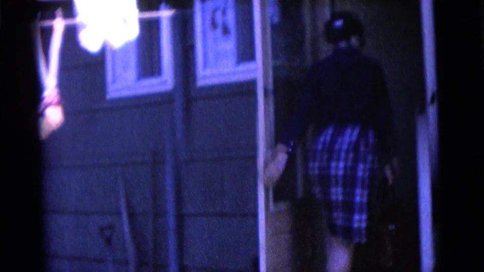 In Camden, New Jersey home-movie footage, a person in a plaid dress appears at a house doorway with blue-shifted 8mm color.
