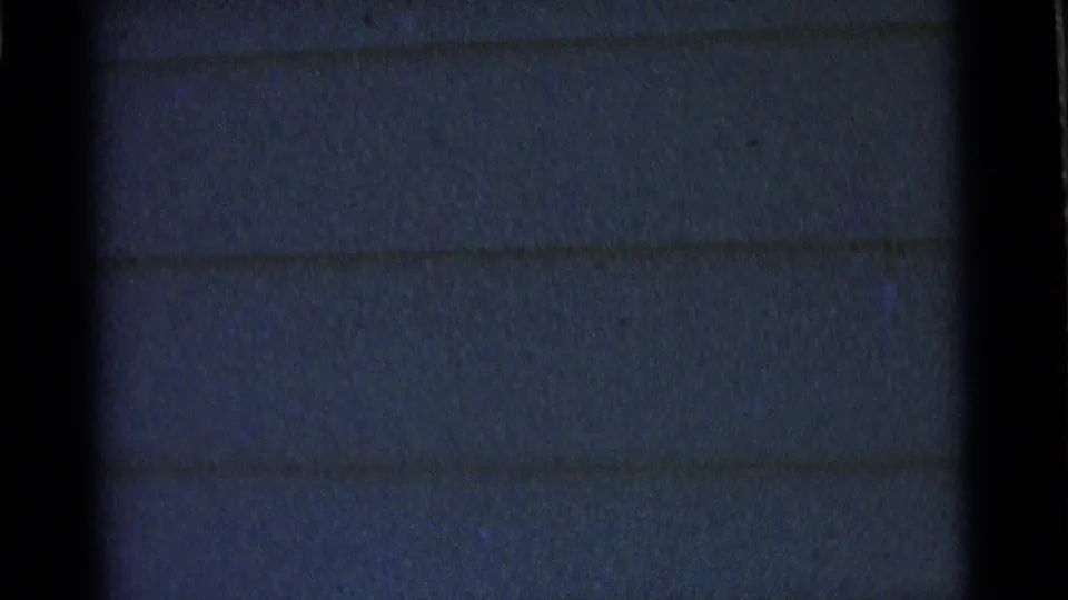 A mostly static 8mm frame shows dark exterior house siding and film borders, with no clear subject in the center.