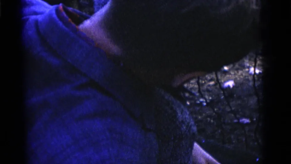 A child in a blue shirt is held close to a wire enclosure in Camden, New Jersey 1961 home-movie footage.
