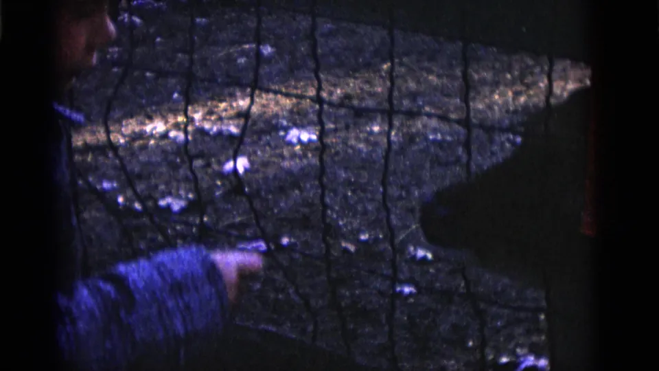 A child and adult remain beside the petting-zoo fence as a dark animal shape moves near the enclosure edge.