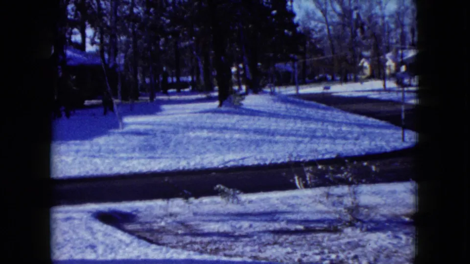 1960 Madison, Wisconsin 8mm frame showing a snowy residential street, lawns, bare trees, and distant houses.
