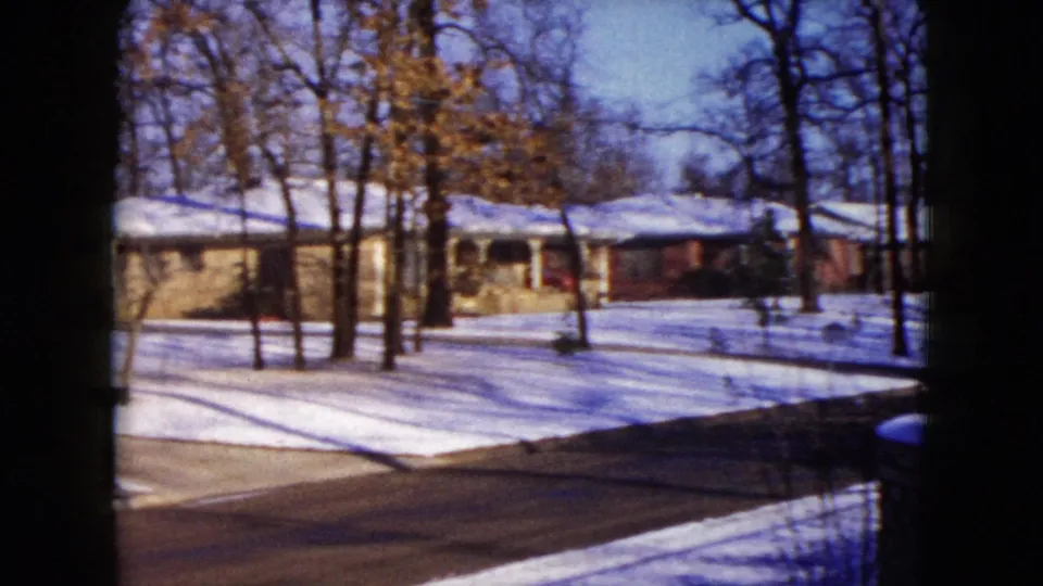 1960 Madison, Wisconsin 8mm view of snow-covered front yards, bare trees, driveways, and low houses beside a residential street.