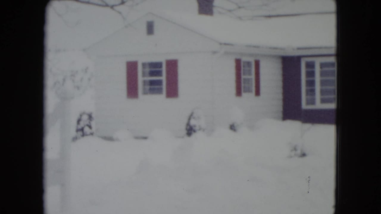 White house facade with red shutters surrounded by deep snow.
