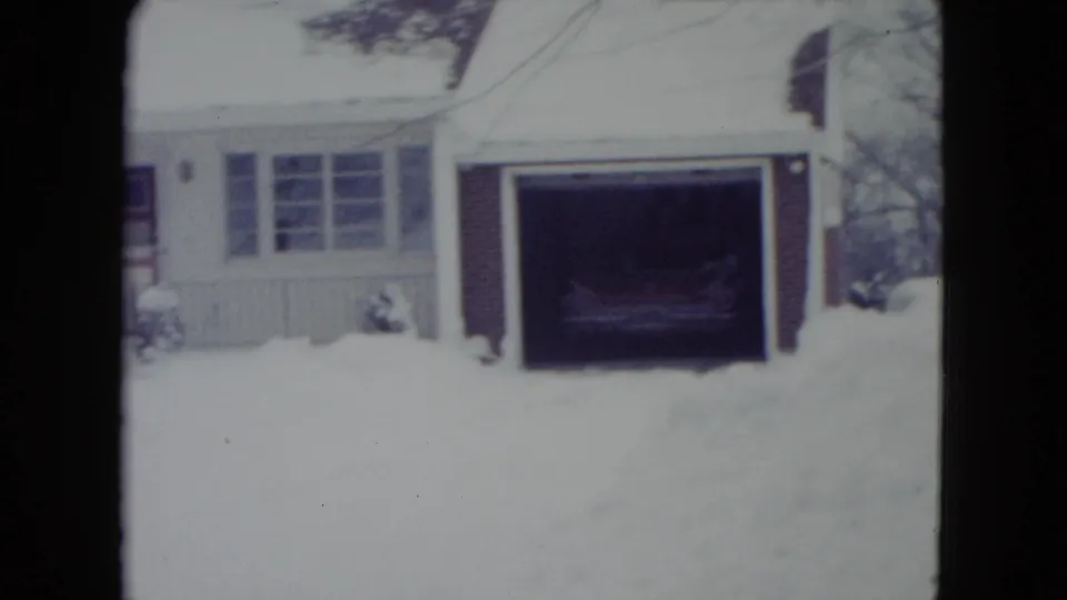 Snowy Madison residence with an open attached garage and a car visible in shadow inside, filmed in a soft 8mm home-movie style.