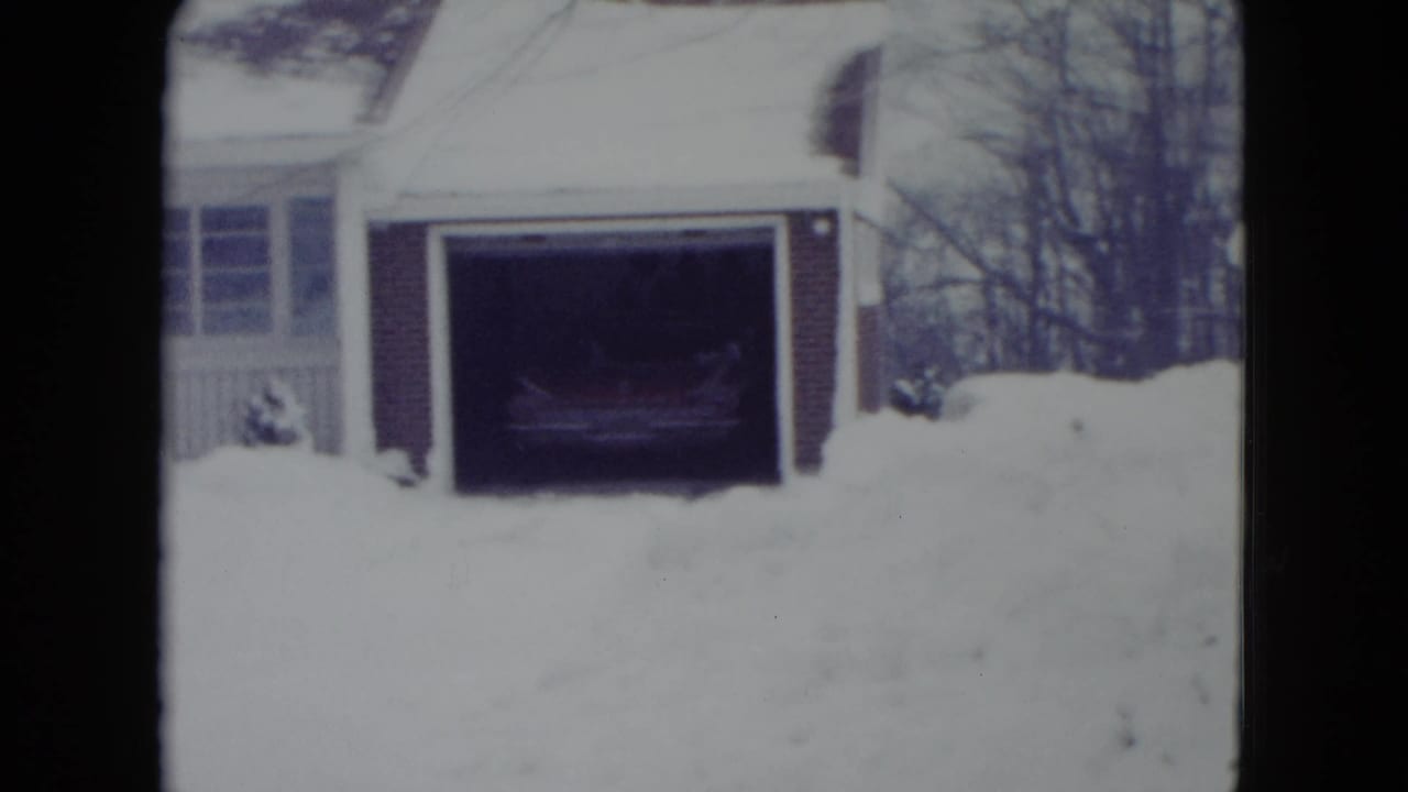 Snow-covered driveway with an open brick garage and a car partly visible inside.