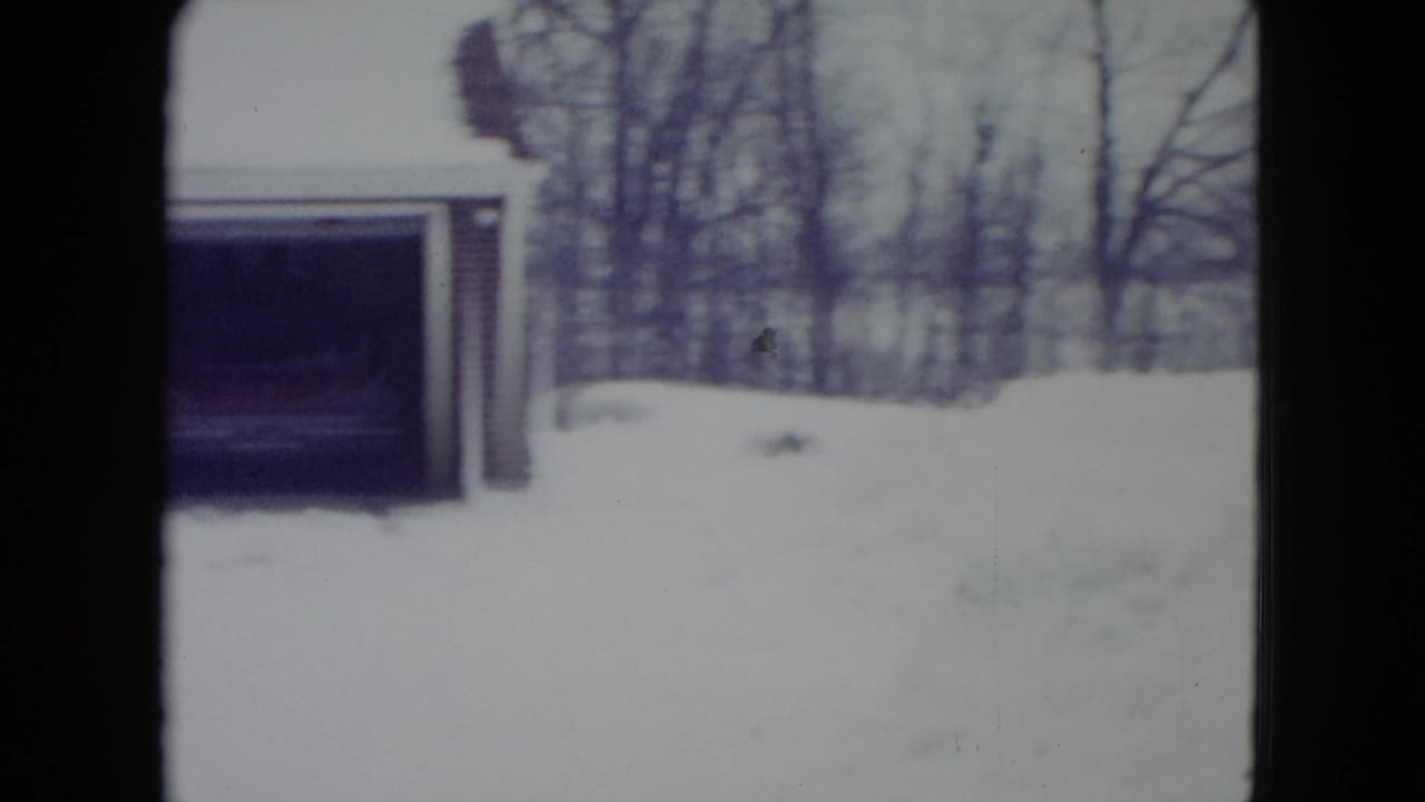 1960 Madison, Wisconsin 8mm frame showing a snowbound suburban house exterior, garage opening, bare trees, and soft faded color.
