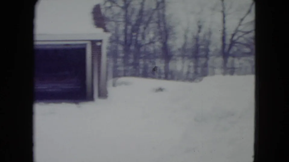 1960 Madison, Wisconsin 8mm frame showing a snowbound suburban house exterior, garage opening, bare trees, and soft faded color.