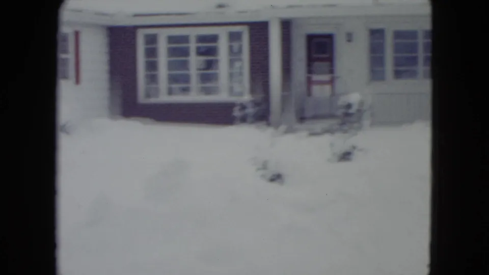 1960 Madison, Wisconsin 8mm view of a snow-covered house front with large windows, shutters, entry door, and porch area.