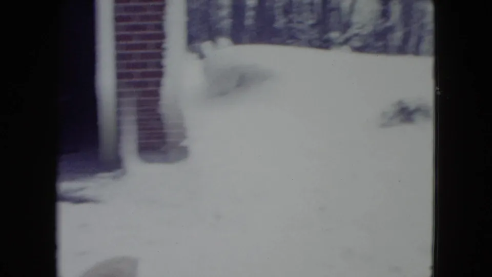 1960 Madison winter frame with a brick building edge, deep snowbank, snowy yard, and leafless trees in the distance.