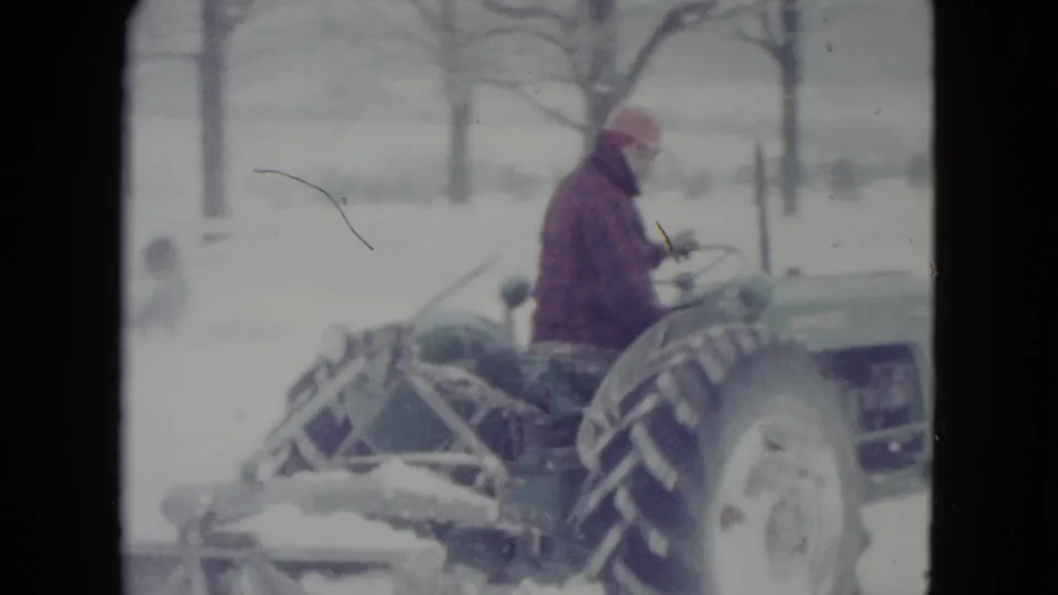 Madison, Wisconsin 8mm frame showing the tractor and operator continuing through a snow-covered rural landscape.