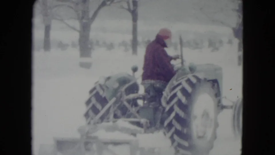 In Madison, Wisconsin archival 8mm footage from 1960, a man in red drives a vintage tractor through a snowy rural area.