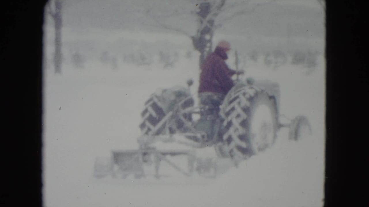 Tractor and driver move across a snowy landscape with a plow behind.