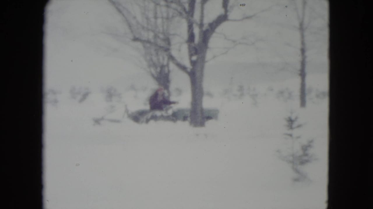 In 1960 Madison, Wisconsin footage, a distant adult drives a vintage tractor through a snowy rural field near leafless trees.