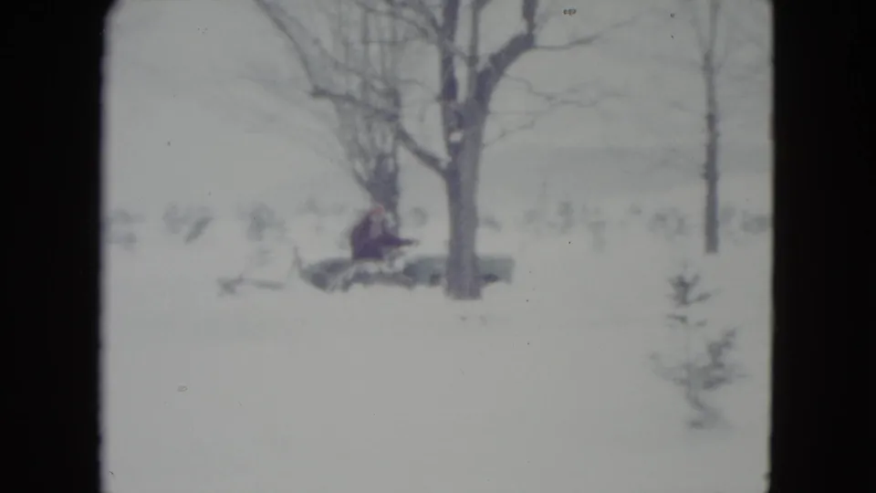 In 1960 Madison, Wisconsin footage, a distant adult drives a vintage tractor through a snowy rural field near leafless trees.