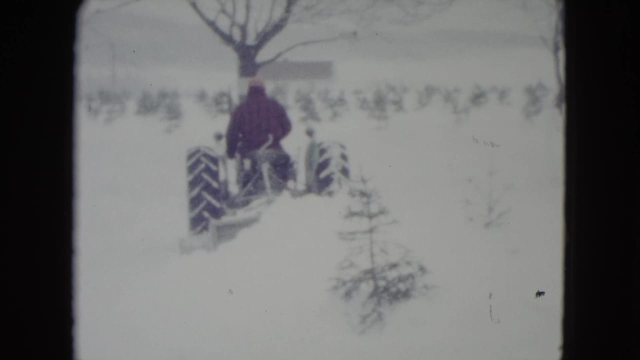 Man drives a tractor away through a snow-covered field.