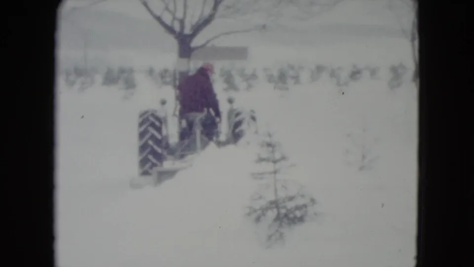 1960 Madison, Wisconsin 8mm frame with the tractor seen from behind as it travels through a snowy rural field.