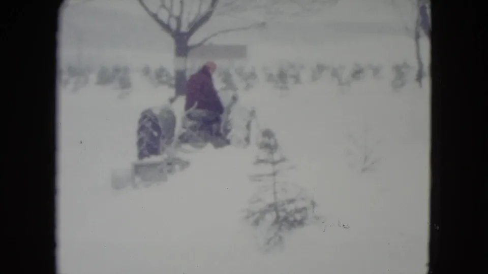 1960 Madison, Wisconsin 8mm frame showing a man on a tractor moving past a small evergreen in deep snow.