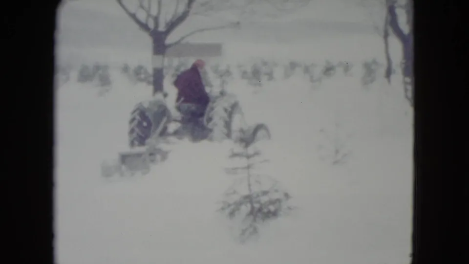 In 1960 Madison, Wisconsin, an adult man drives a vintage tractor with a blade through a snowy field.