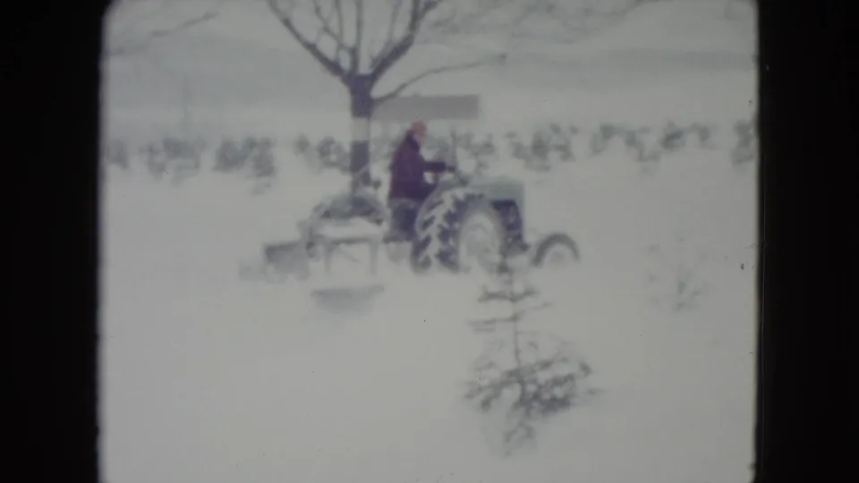 In Madison, Wisconsin, 1960, a bundled adult operates a small tractor with a blade implement across a snowy field.