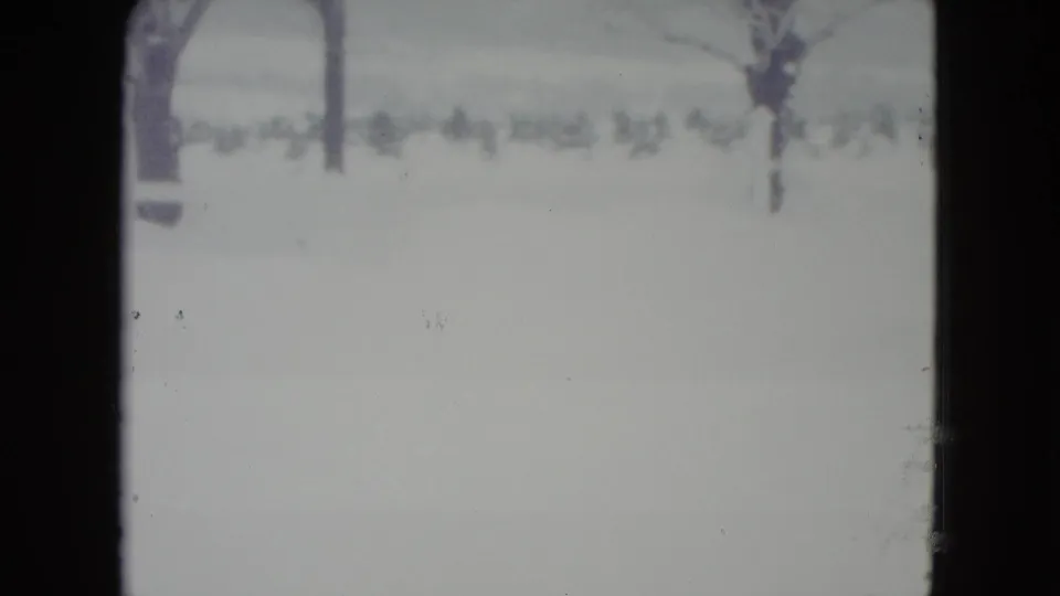 Madison, Wisconsin winter home-movie frame showing a snowy field and bare trees, with no tractor visible yet.