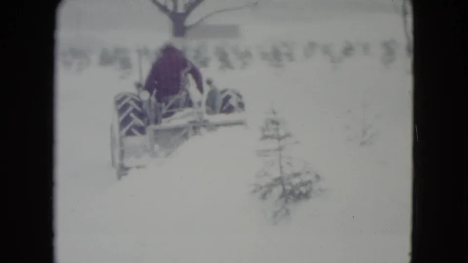 In Madison, Wisconsin, a man in a red jacket drives a vintage tractor with a blade implement through deep snow.