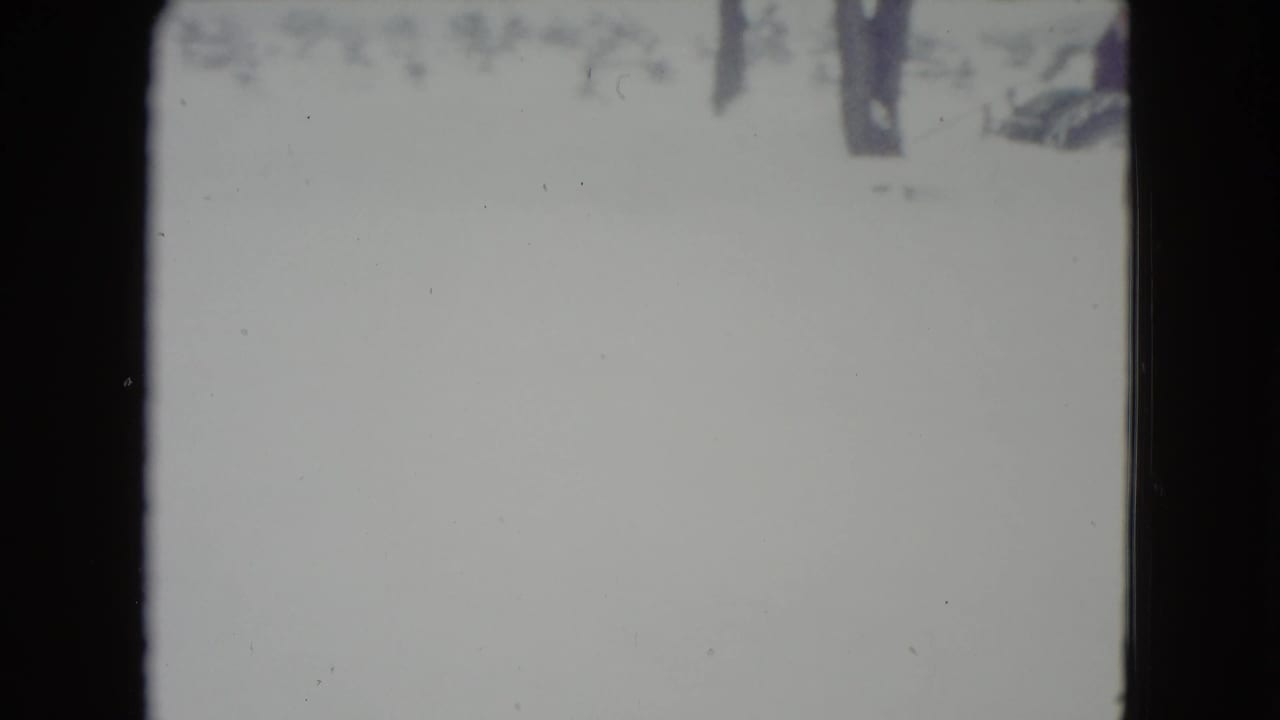 Snowy field with bare trees and dark film borders; no clear person or tractor visible in this frame.