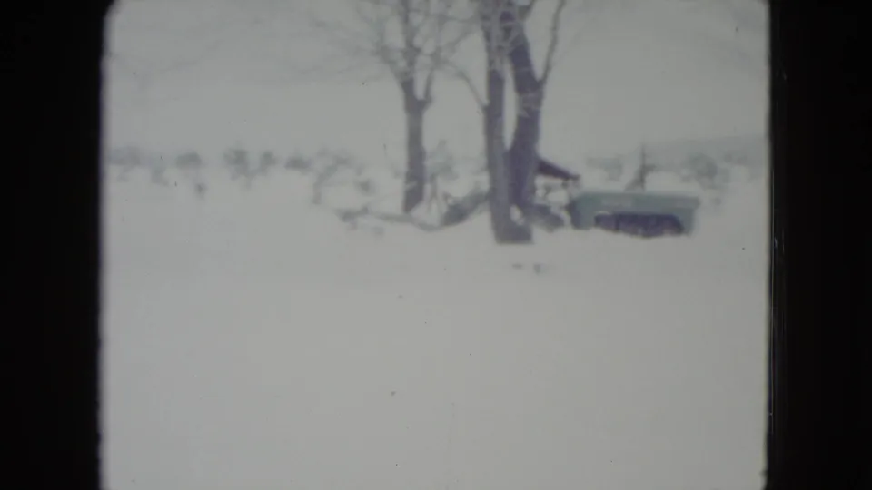 1960 Madison, Wisconsin 8mm frame showing a snow-covered yard, bare trees, and a small plow or tractor beyond the foreground snow.