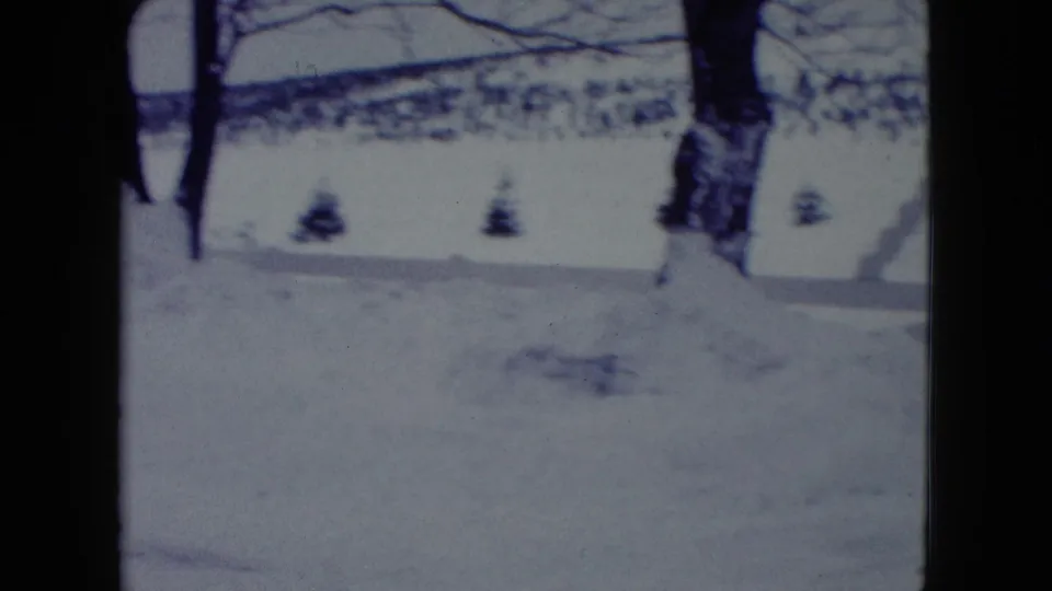 1960 Madison home-movie frame showing a snow-covered residential yard with bare trees, small shrubs, and deep winter snow.