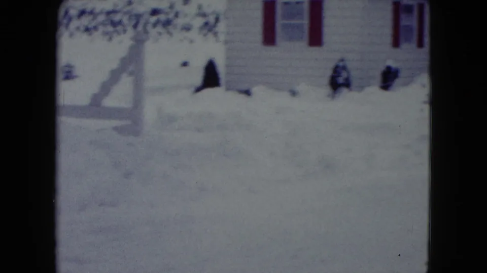 Snow piles cover the yard beside a Madison residential house with red shutters and shrubs visible in the home-movie frame.