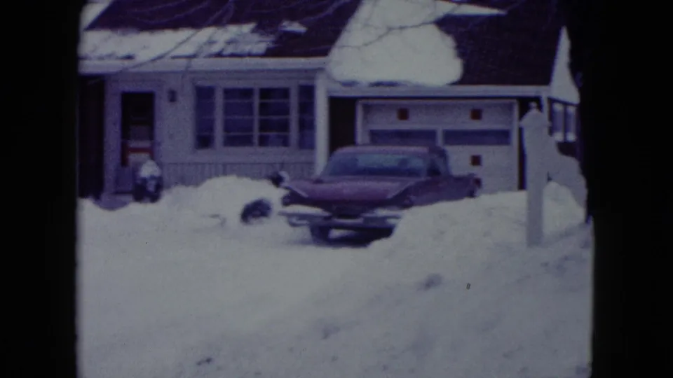 A period car sits in a snow-covered driveway beside a garage at a Madison residential house in the 8mm footage.