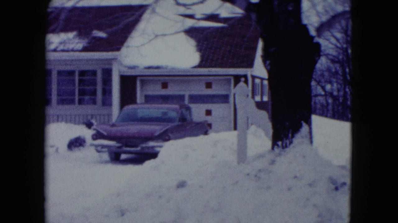 Red vintage car parked in a snowy driveway beside a suburban house.