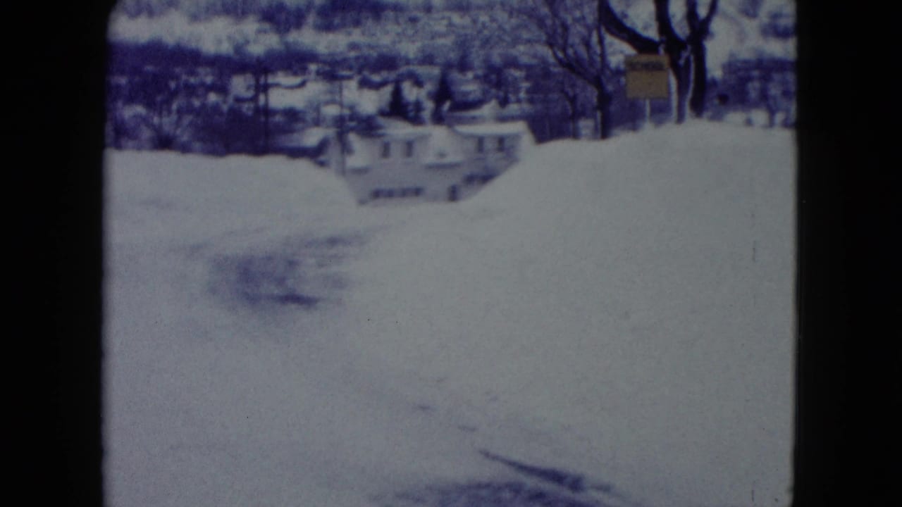 Snowy residential street with high snowbanks and houses in the distance.