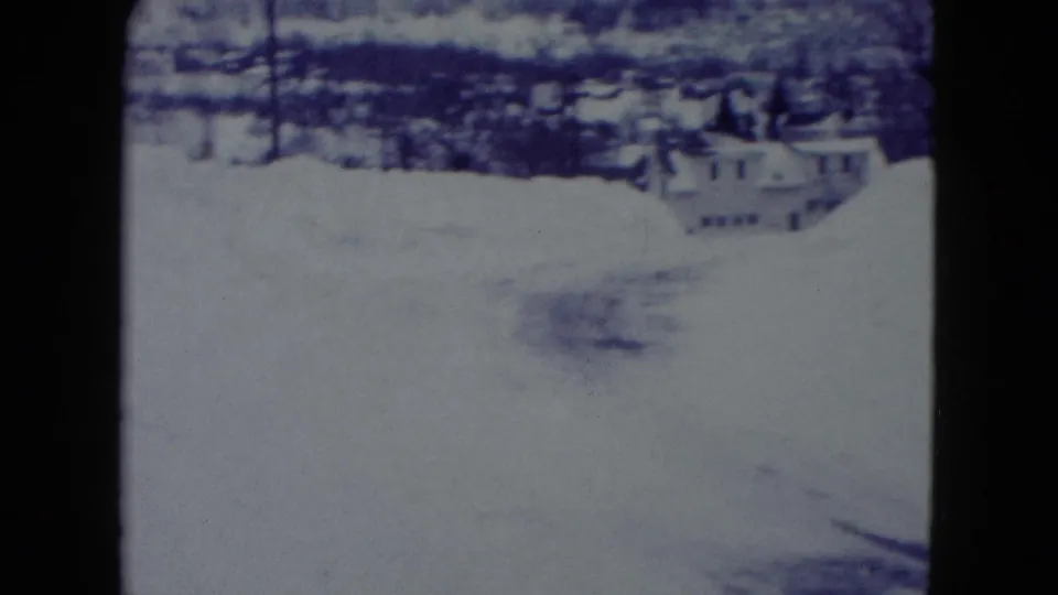 Soft 8mm frame of a Madison, Wisconsin winter street, with deep snowbanks and distant residential houses visible.