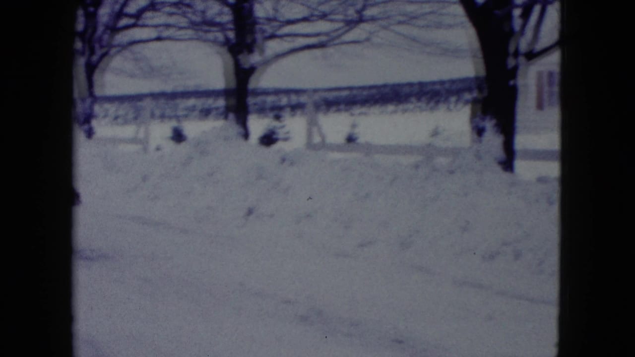 A 1960 Madison winter yard appears under deep snow, with bare trees, snowbanks, and part of a residential house at frame right.