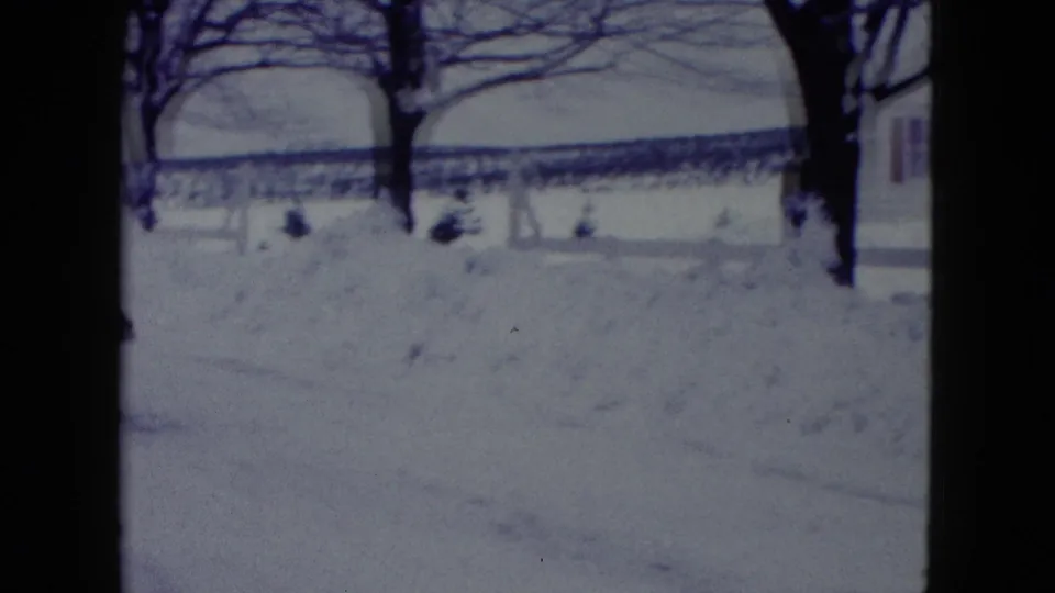 A 1960 Madison winter yard appears under deep snow, with bare trees, snowbanks, and part of a residential house at frame right.